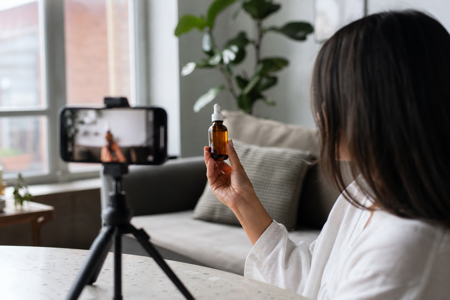 UGC creator filming a product sample video on a phone tripod by a window